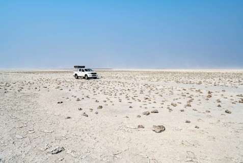 Four-wheel drive Toyota Hilux with roof tent, driving over salt pan, lone car in large wide plain,
