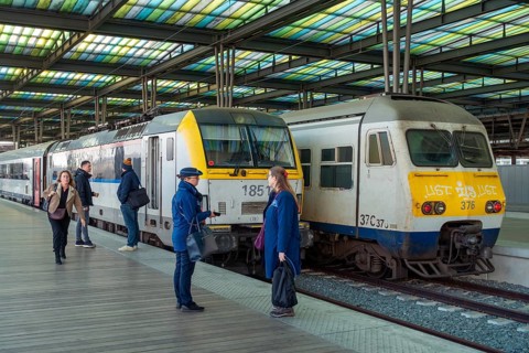 Passengers and two railway employees, ticket inspectors in front of waiting trains on platform at