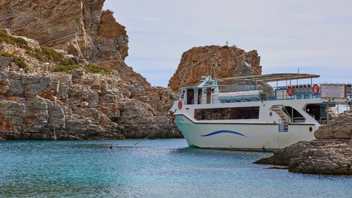 Palatia Beach, Palatia, A boat anchored near a rocky shore in clear blue water under a calm sky,