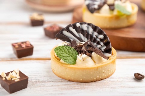 Sweet tartlets with chocolate and cheese cream with cup of coffee on a white wooden background and