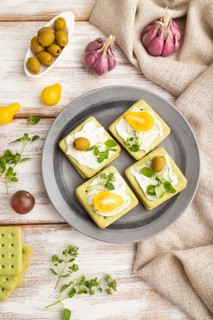 Green cracker sandwiches with cream cheese and cherry tomatoes on white wooden background and linen