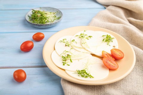 White cheese with tomatoes and cilantro microgreen on blue wooden background and linen textile.