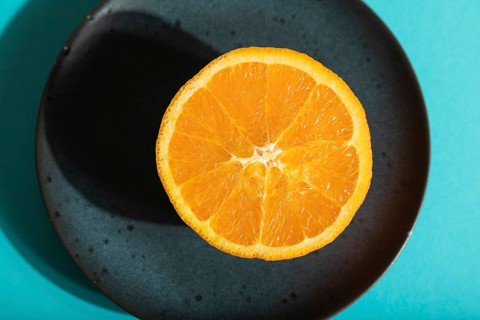Ripe cut orange on blue ceramic plate on blue pastel background. Top view, flat lay, close up, hard