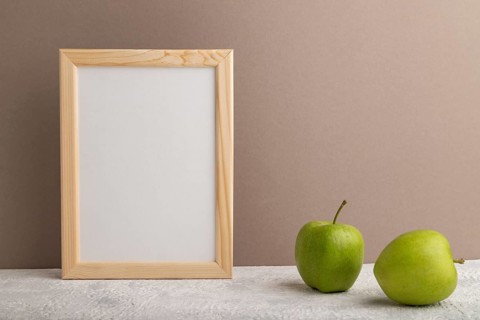 White wooden frame mockup with green apple on beige paper background. Blank, vertical orientation,