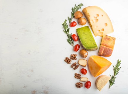 Set of different types of cheese with rosemary and tomatoes on a white wooden background. Top view,