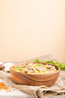 Lentils porridge with champignons and coriander in a wooden bowl on a white and orange background