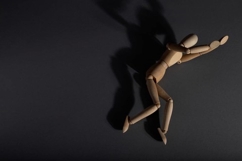 Wooden mannequin lies in a protective position on gray background. loneliness, violence,