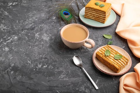 Homemade honey cake with milk cream and mint with cup of coffee on a black concrete background and