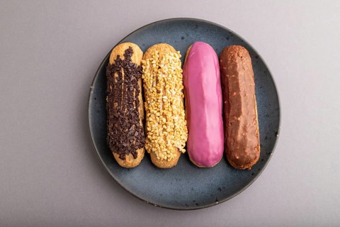 Set of eclair, traditional french dessert on blue ceramic plate on gray pastel background. top
