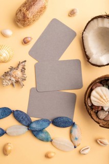 Brown paper business card with coconut, seashells, pebbles, beads on orange pastel background. Top