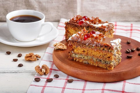 A piece of cake with caramel cream and poppy seeds on a wooden kitchen board and a cup of coffee,