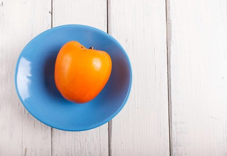 Ripe orange persimmon in a blue plate on white wooden background, with copy space