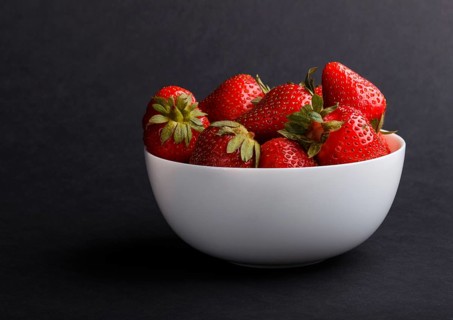 Fresh red strawberry in white bowl on black background. side view, close up