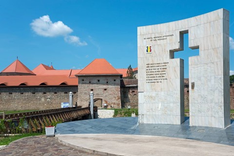 A modern monument with cross and inscription against the backdrop of an old fortress, Fortress and