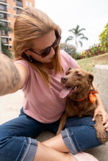 A selfie of a woman looking at her pet, a brown-furred dog with a bindi on its third eye, sticking