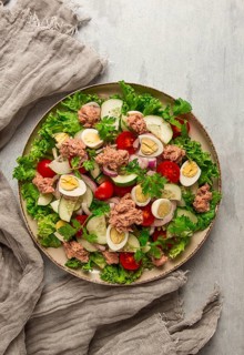 Tuna salad, vegetable salad with quail eggs, lettuce, red onion and cucumbers, on a light gray