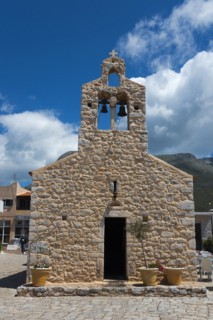 A traditional stone church with a bell tower under a clear blue sky and mountains in the
