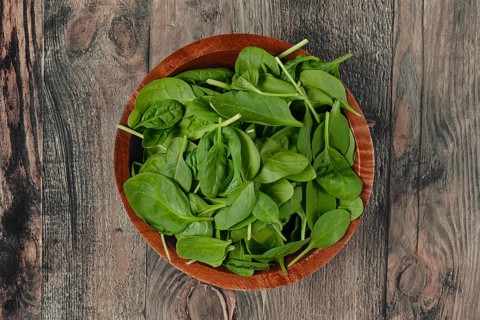 A wooden bowl with vibrant, fresh and crisp spinach leaves on a rustic wooden table, ideal for