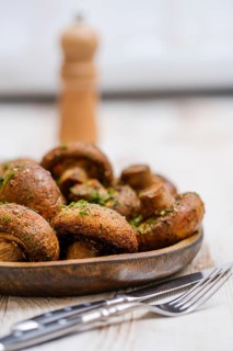 A wooden plate displays a heap of freshly cooked mushrooms seasoned with herbs, accompanied by a