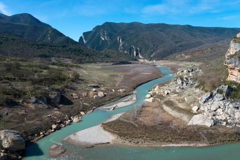 A clear jade river flows through a wide valley, surrounded by dramatic cliffs and wooded mountains