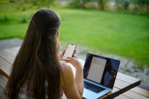 A multitasking woman using a laptop and smartphone in a serene garden setting while working on