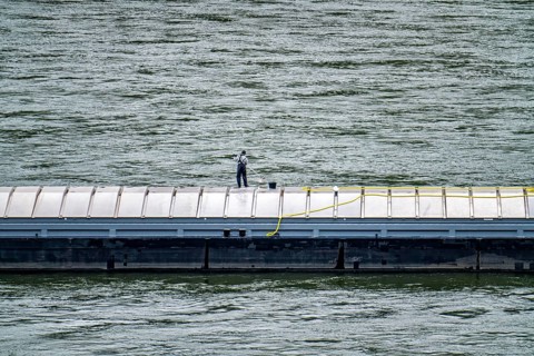 Inland waterway vessel, freighter, with closed cargo hatches, employee cleans the deck with water