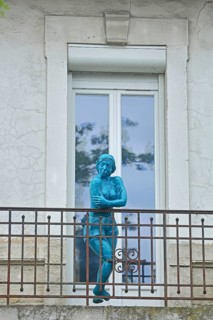 Sculpture by Nicole Brousse, blue woman on balcony railing in front of door, window, blue,