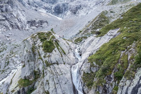 Aerial view, hikers on bridge over glacial stream, large single rock, hiking path from La Fouly to