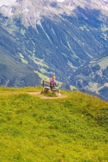 A woman sits on a bench and observes the sweeping valleys and green hills, Penken, Zillertal,