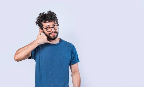 Attractive young man imitating telephone conversation isolated. Young man in glasses making calling