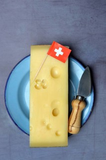 A piece of Swiss Emmental cheese on a plate and the Swiss flag