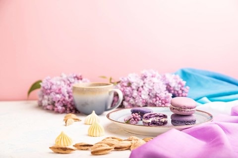 Purple macarons or macaroons cakes with cup of coffee on a white and pink background and
