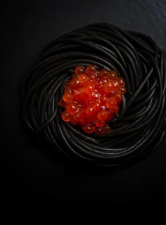 Black spaghetti with red caviar, pasta, on a black background, top view, no people
