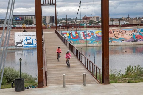 Pueblo, Colorado, Bicycle riders cross a bridge over the Arkansas River where murals and a bike