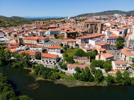 Historic city with red roofs and a dominant cathedral, surrounded by lush hills and a river in the