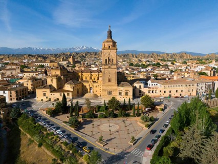 Historic town with a large church in the centre, surrounded by mountains and sunny skies. Trees and