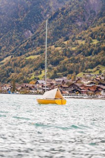 A yellow sailing boat rocks on the lake in front of a picturesque village on the mountain, Lake