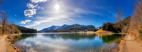 Clear mountain lake in quiet, sunny surroundings with reflecting water surface and forest backdrop,