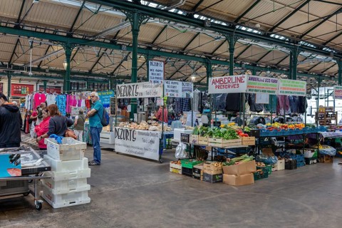 Busy indoor market filled with vegetable and clothing stalls and people, Belfast