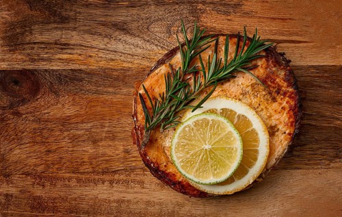 Salmon steak, fried, on a cutting board, top view, rosemary, lemon and lime, homemade, one serving,