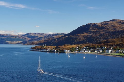 Coastal view with a sailing boat, village and hills in the background under a clear sky, autumn,