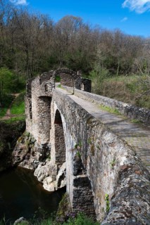 Historische Steinbrücke, die über einen Fluss führt, umgeben von Wald und Ruinenresten unter einem
