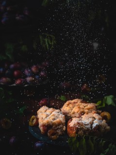Plum cake on a plate, dusted with icing sugar in a dark, rustic autumn setting with plums and