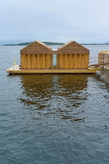 Outdoor sea pool by the fjord with small wooden sauna huts, overcast sky and calm water, Molde,