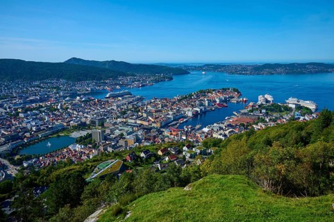 Panoramic view of a coastal town with harbour and a variety of buildings, surrounded by mountains