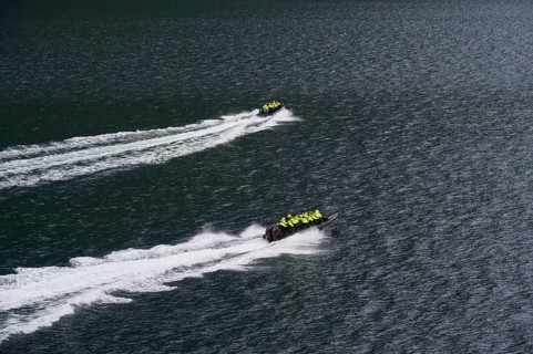 Two speedboats with groups of people travelling fast in the Geiranger Fjord, white waves are coming