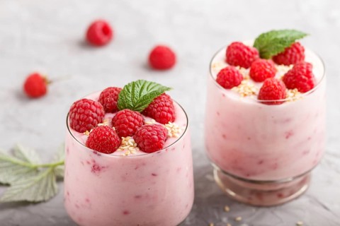 Yoghurt with raspberry and sesame in a glass and wooden spoon on gray concrete background. side