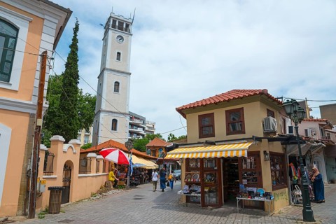 View of a busy street with a white bell tower and Mediterranean-style shops, clock tower,