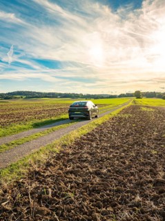 A car drives on a country lane between fields under a sky with clouds at sunset, car sharing, VW