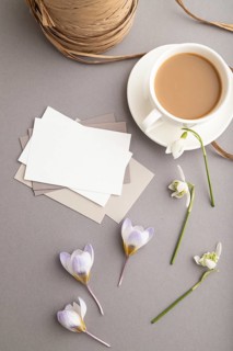 White paper business card mockup with spring snowdrop crocus and galanthus flowers and cup of